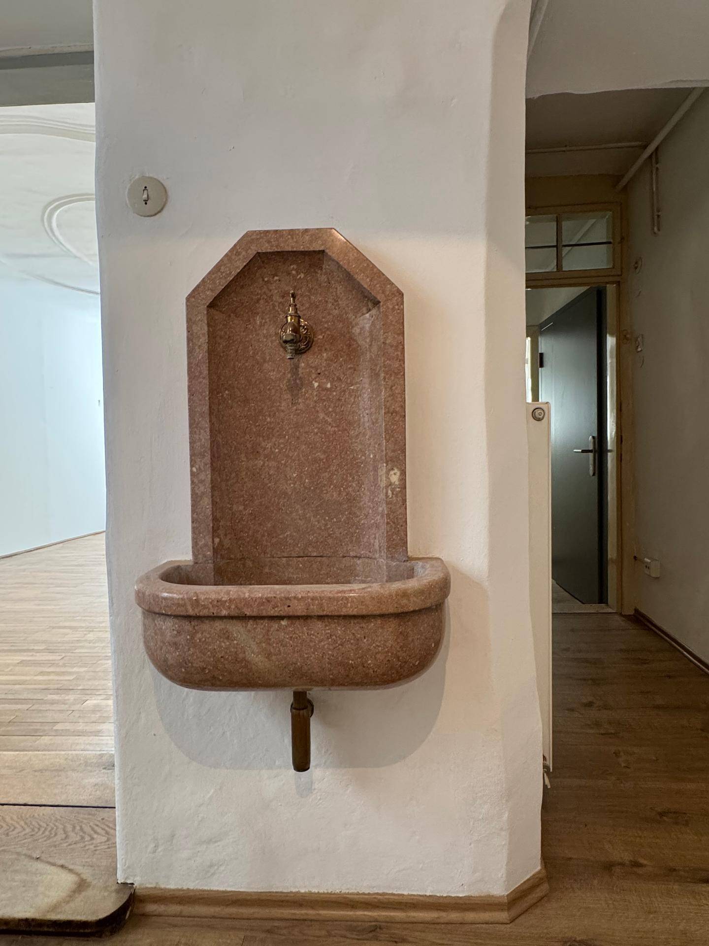 Detailansicht eines traditionellen Wandbrunnens aus Stein in einem historischen Flur.