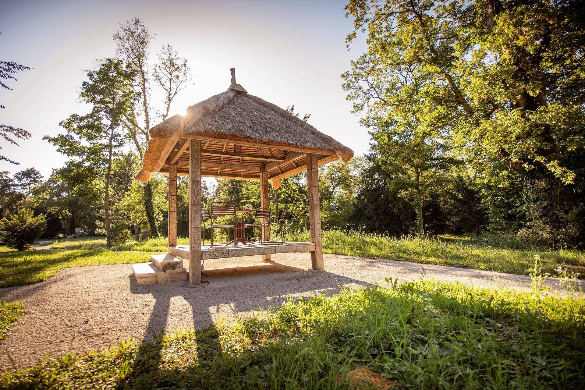 Romantischer Pavillon mit Strohdach in einem weitläufigen Park, ideal zum Entspannen.