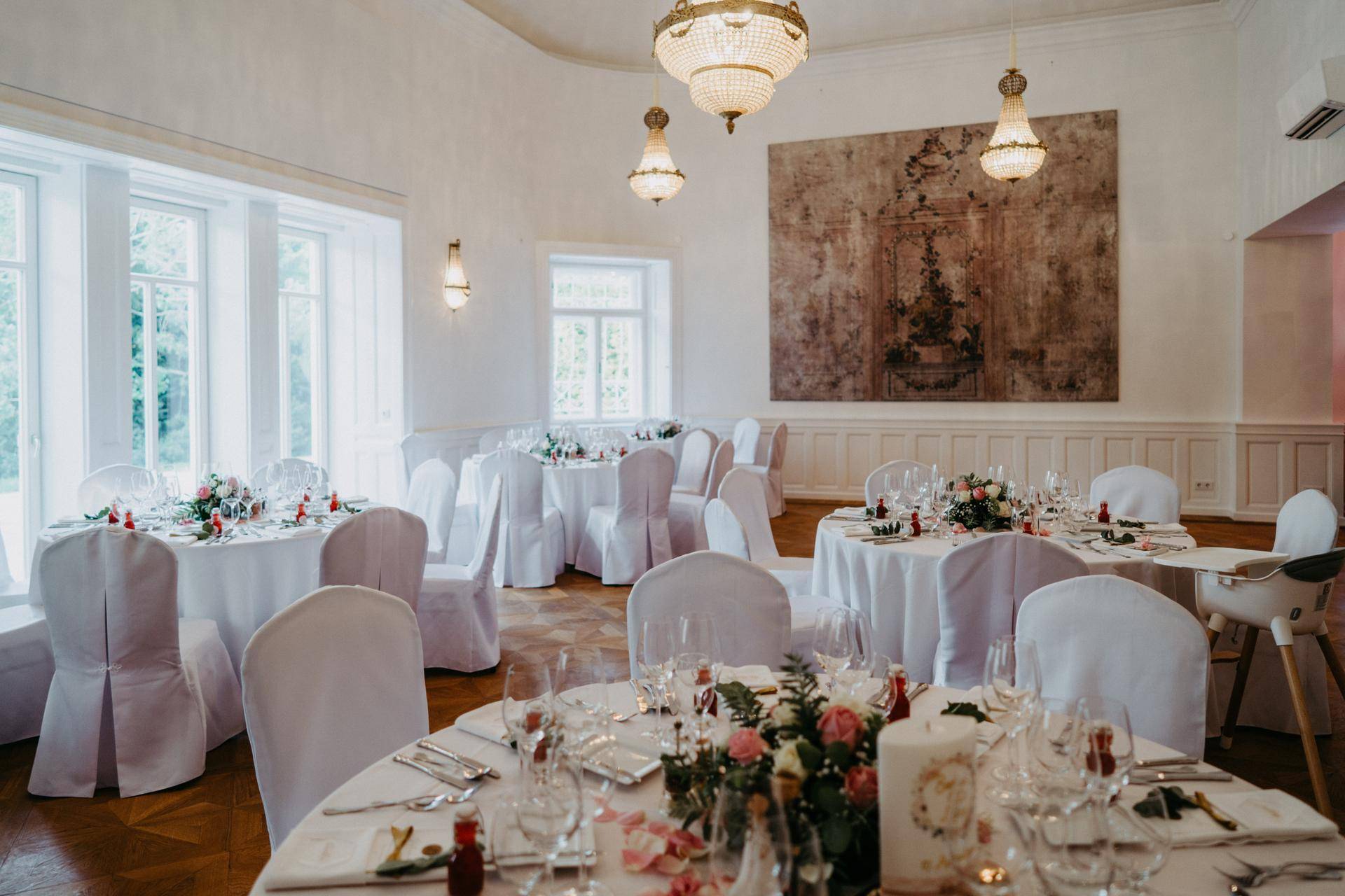 Festlich gedeckter Speisesaal mit großen Fenstern, Kronleuchtern und eleganten Tischdekorationen.