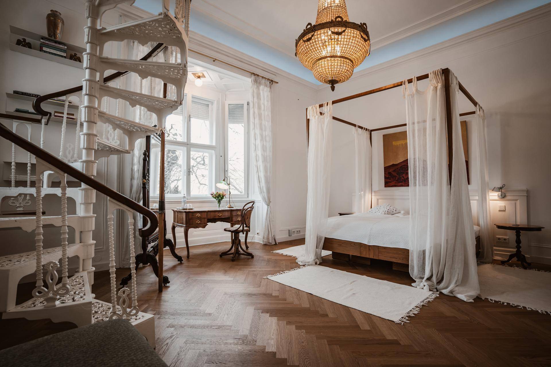 Elegantes Schlafzimmer mit Himmelbett, Wendeltreppe und Fischgrätparkett.