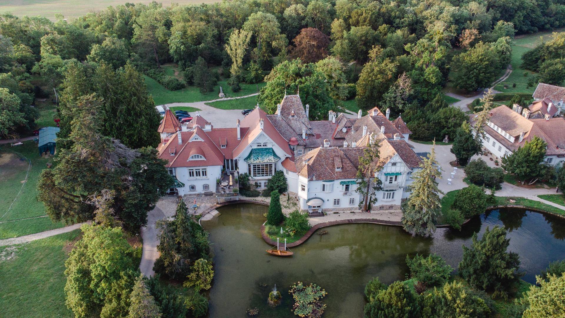 Luftaufnahme eines weitläufigen Anwesens mit großem Gebäude, Teich und üppiger Vegetation.
