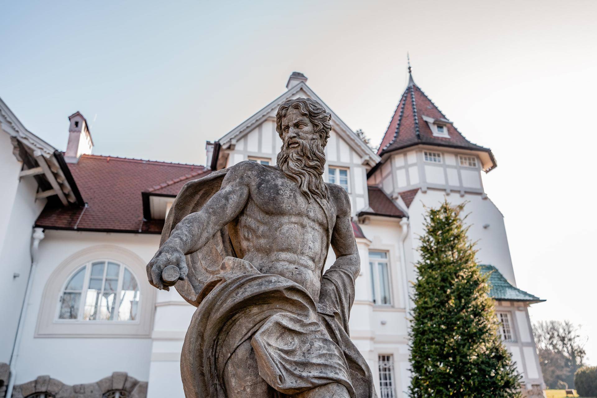 Antike Statue vor der historischen Architektur eines weißen Gebäudes mit roten Dächern.
