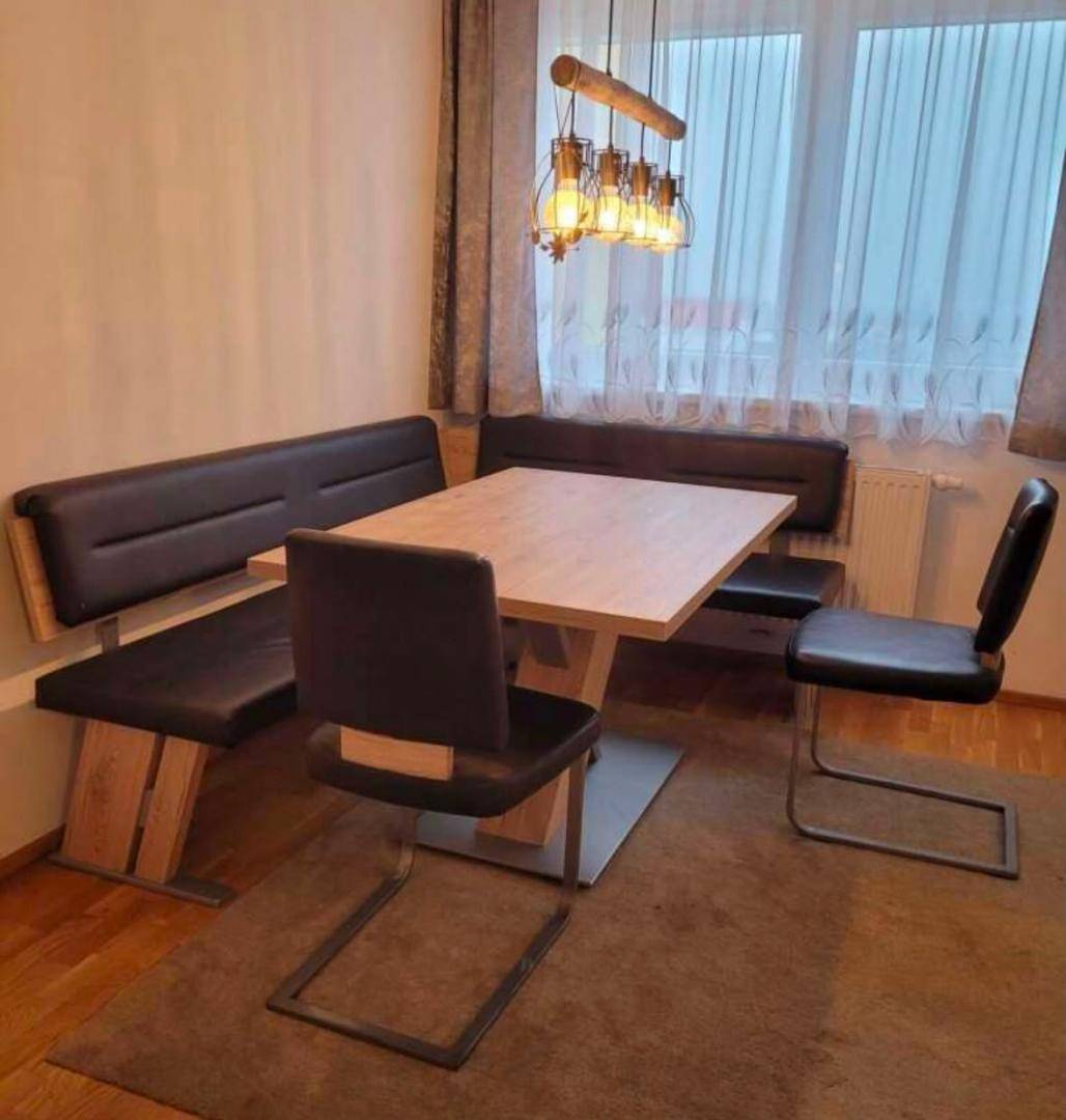 Essbereich mit Eckbank, Esstisch und Stühlen, ergänzt durch einen Teppich auf Holzfußboden.