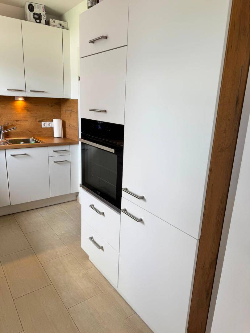 Küchenzeile mit integriertem Backofen, hohen weißen Schränken und Fliesenboden.