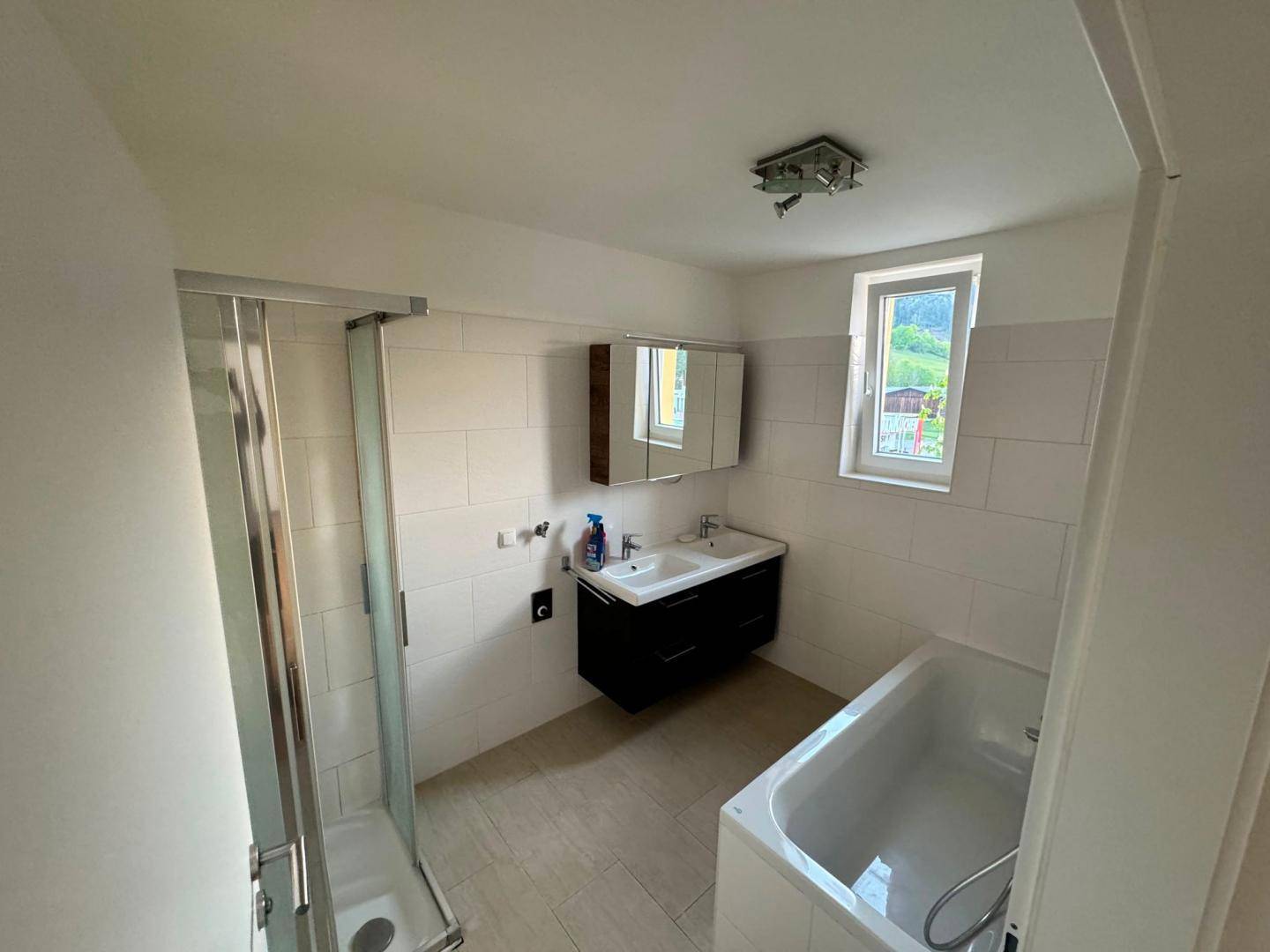 Modernes Badezimmer mit Dusche, Badewanne, Einzelwaschbecken und einem Fenster.