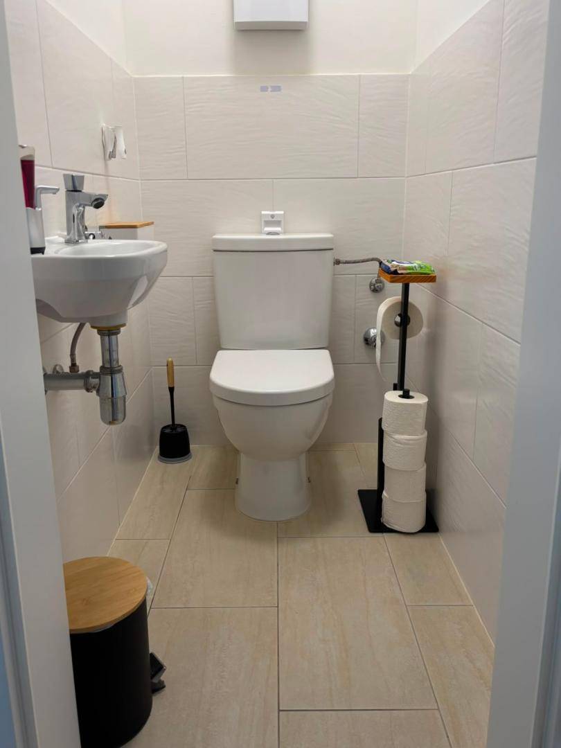 Kleines Gäste-WC mit Toilette, Handwaschbecken und hellen Fliesen an Wänden und Boden.