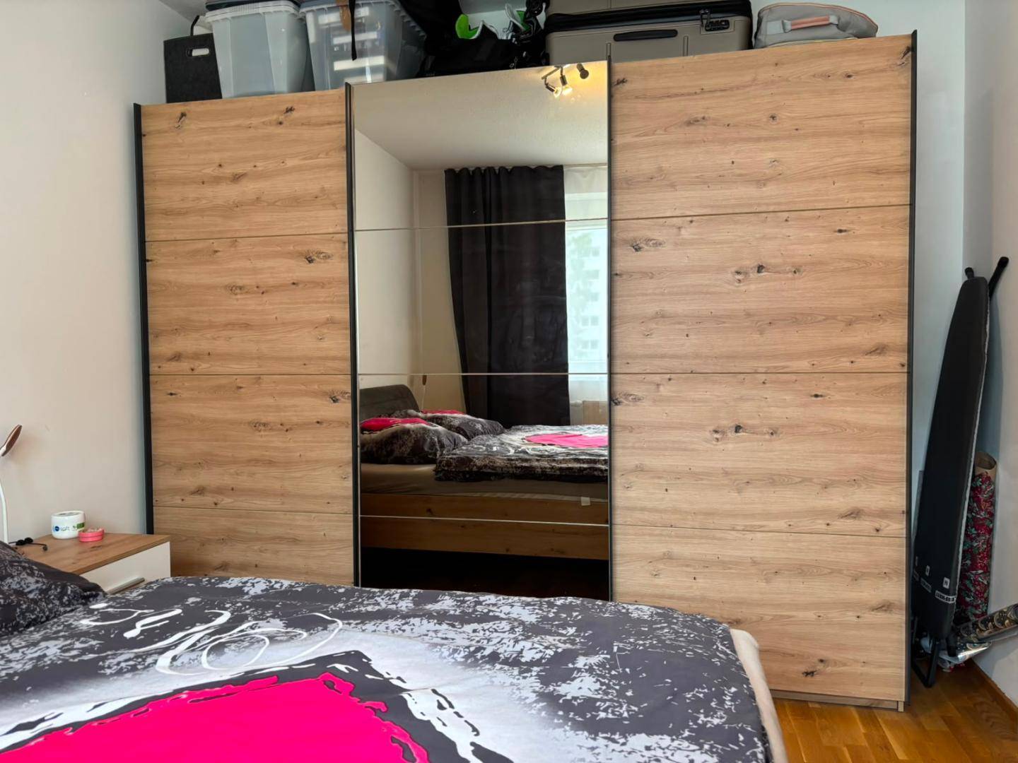 Schlafzimmer mit großem Holzschrank und Spiegeltüren, die das Bett reflektieren.