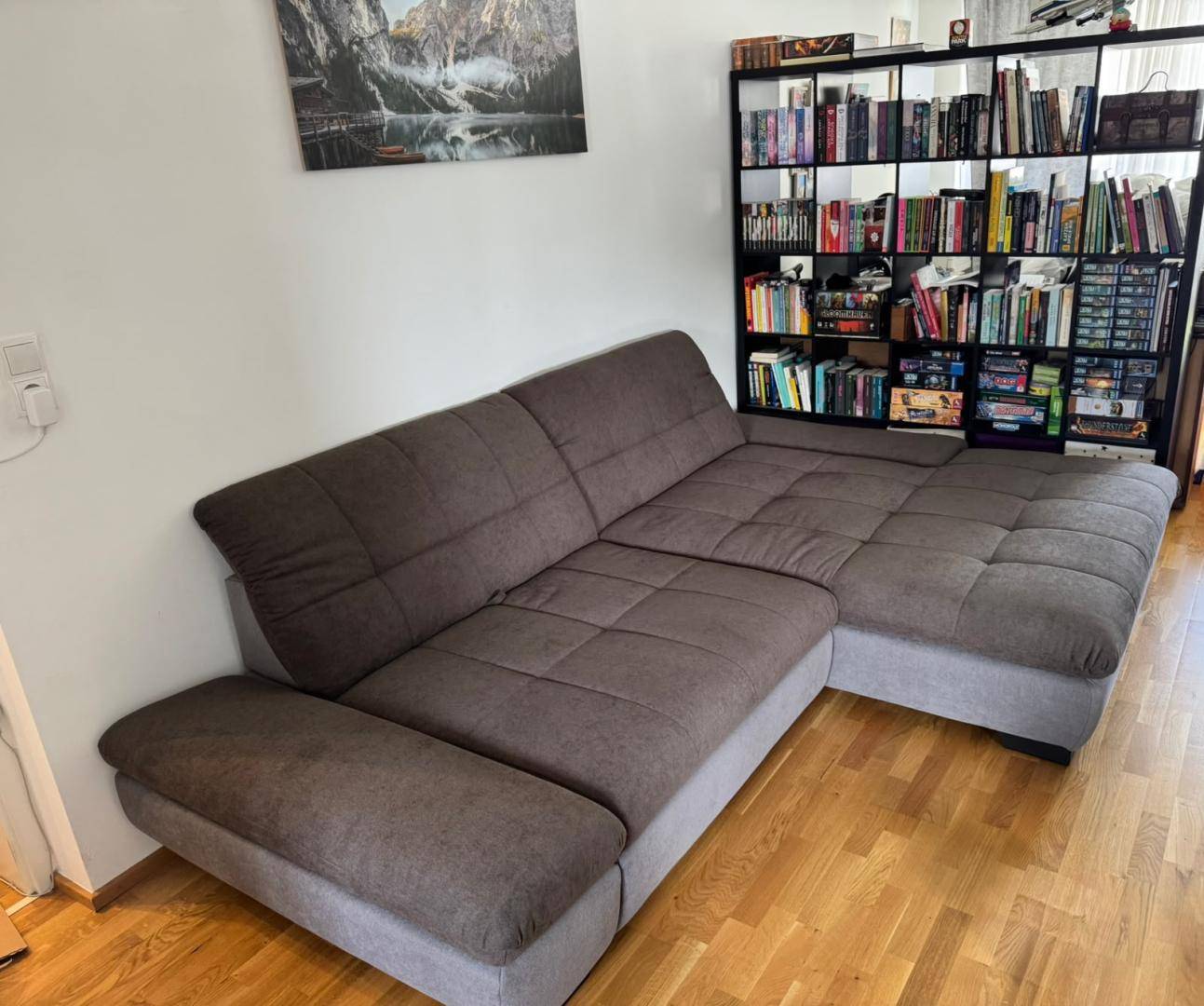 Gemütliches Wohnzimmer mit großem Ecksofa und einem Bücherregal auf Holzfußboden.