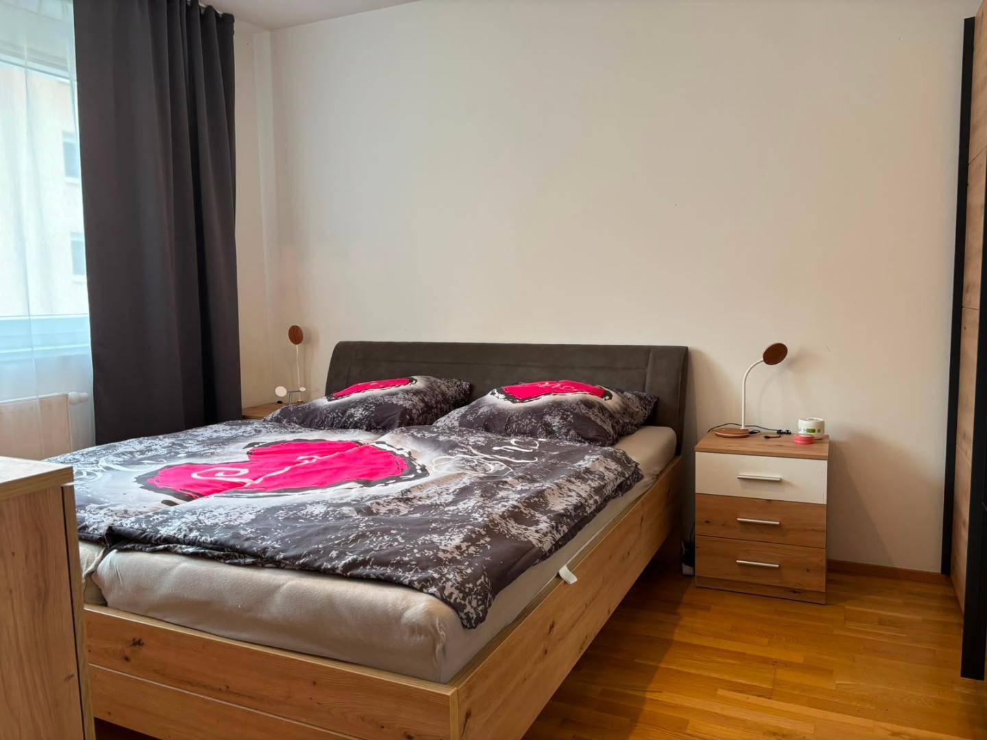 Schlafzimmer mit Holzbettrahmen, Nachttischen und einem warmen Holzfußboden.
