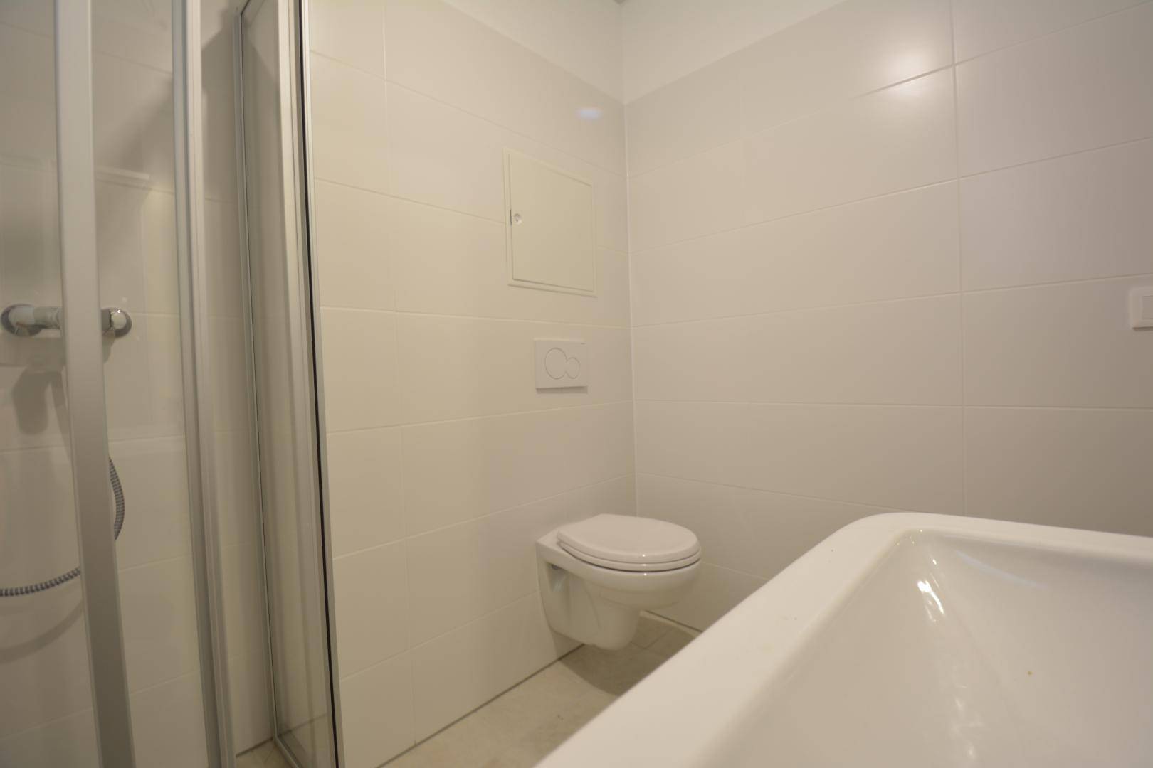 Helles Badezimmer mit Duschkabine, wandhängendem WC und weißen Fliesen, in gutem Zustand.
