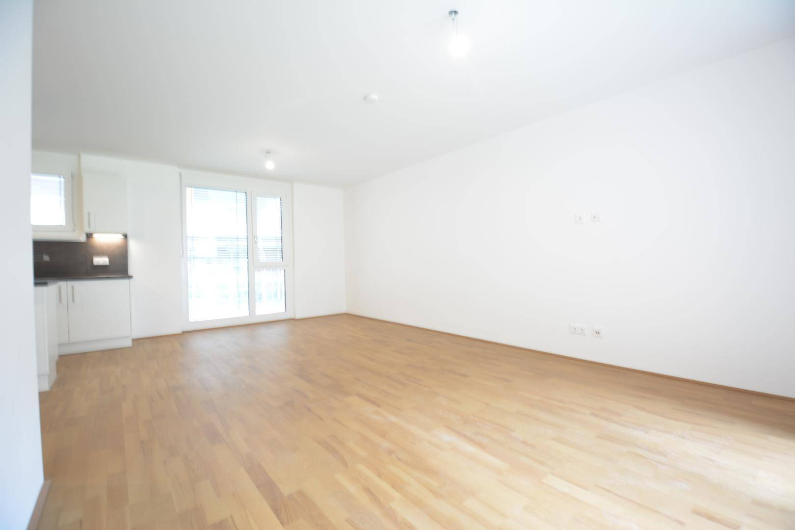 Heller und geräumiger Wohnbereich mit Parkettboden und Zugang zu einem Balkon durch große Fenster.