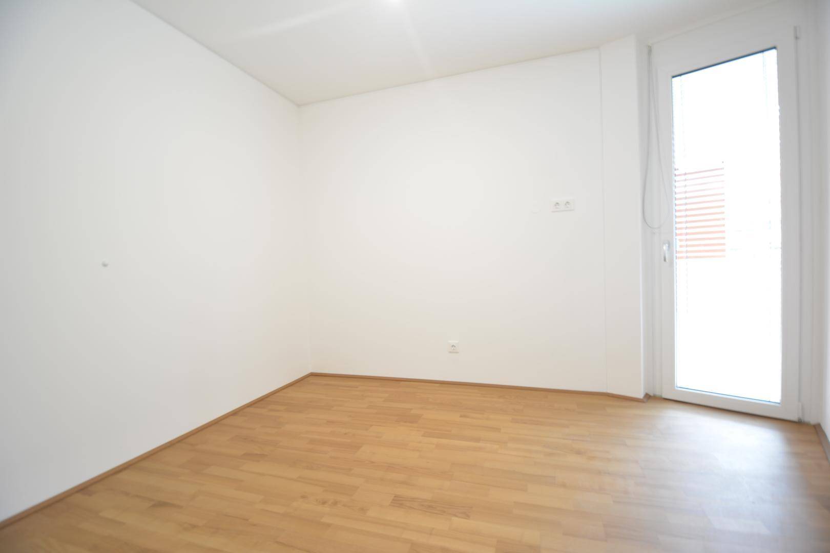 Freundliches Zimmer mit Parkettboden und einer Fenstertür, die Zugang zu einem Außenbereich bietet.