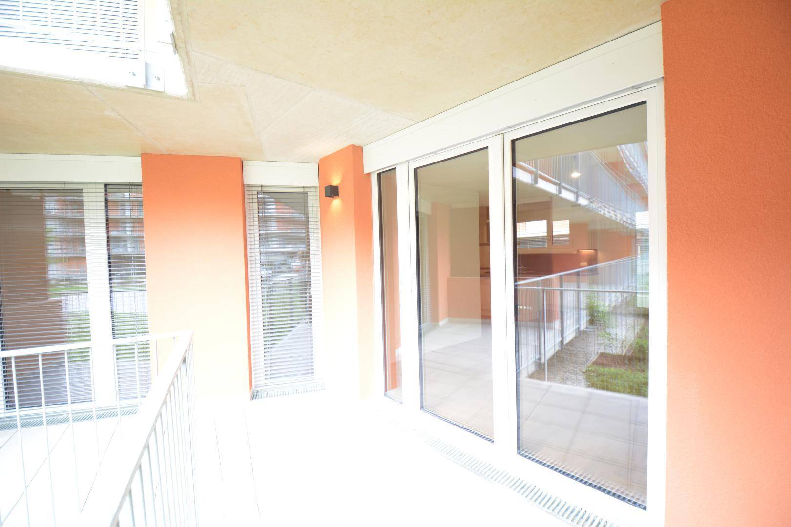 Heller Balkon mit orangefarbenen Wänden und Glasgeländer, bietet einen Blick auf die Umgebung.