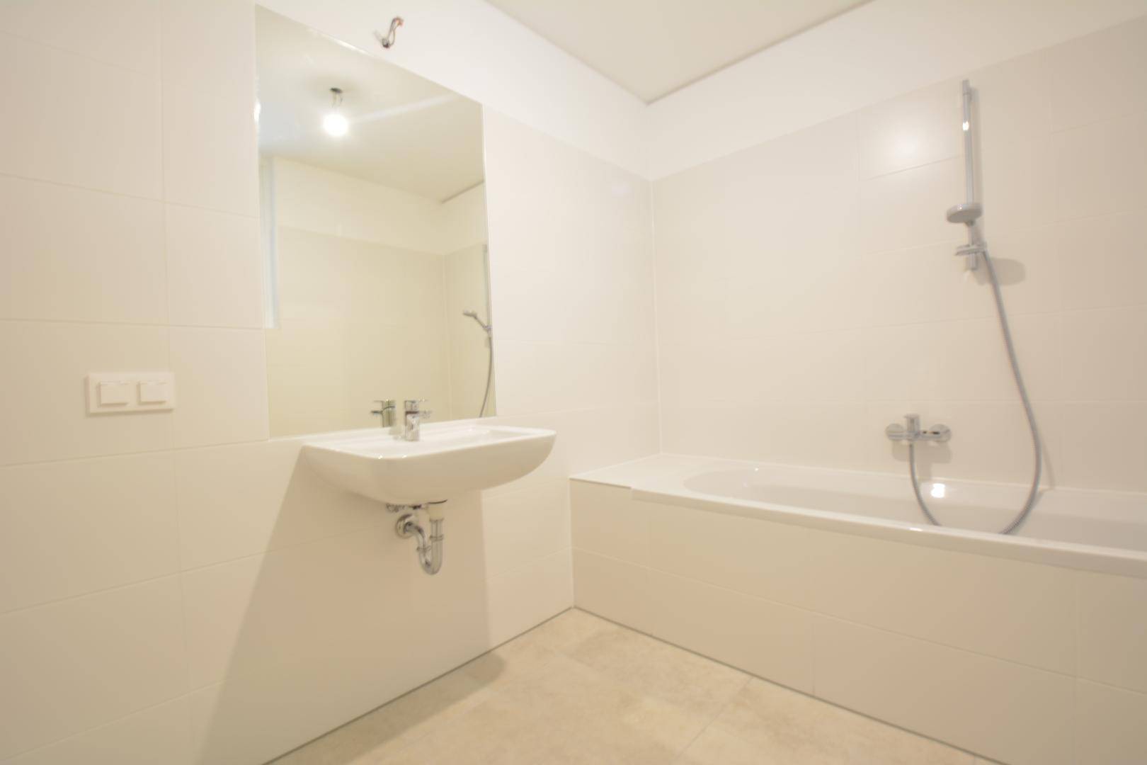 Modernes Badezimmer mit Badewanne, Waschbecken und großem Spiegel, vollständig gefliest.