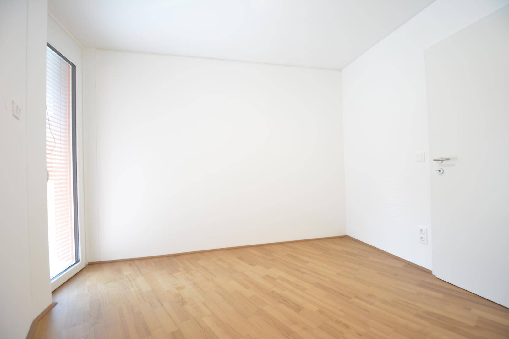 Leeres Zimmer mit hellem Parkettboden und einer Tür, bereit zur individuellen Gestaltung.
