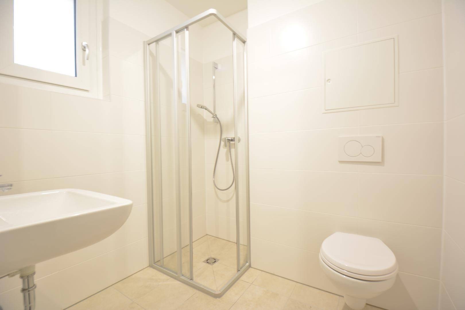 Modernes Badezimmer mit Duschkabine, WC und Waschbecken, komplett gefliest in Weiß.