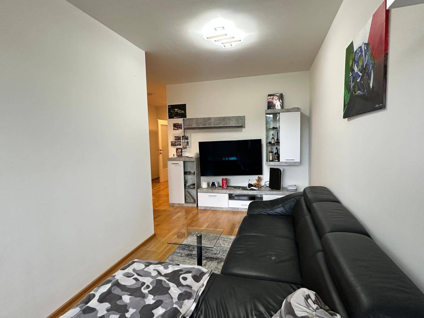 Wohnzimmer mit schwarzem Ledersofa, Fernseher und modernen Möbeln an der Wand.