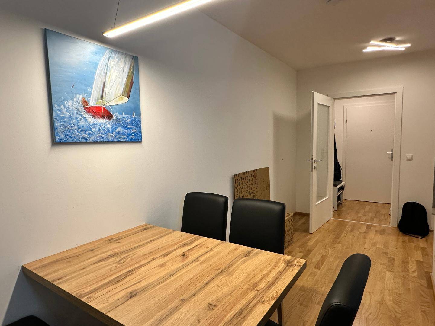 Gemütlicher Essbereich mit Holztisch, schwarzen Stühlen und einem Gemälde an der Wand.