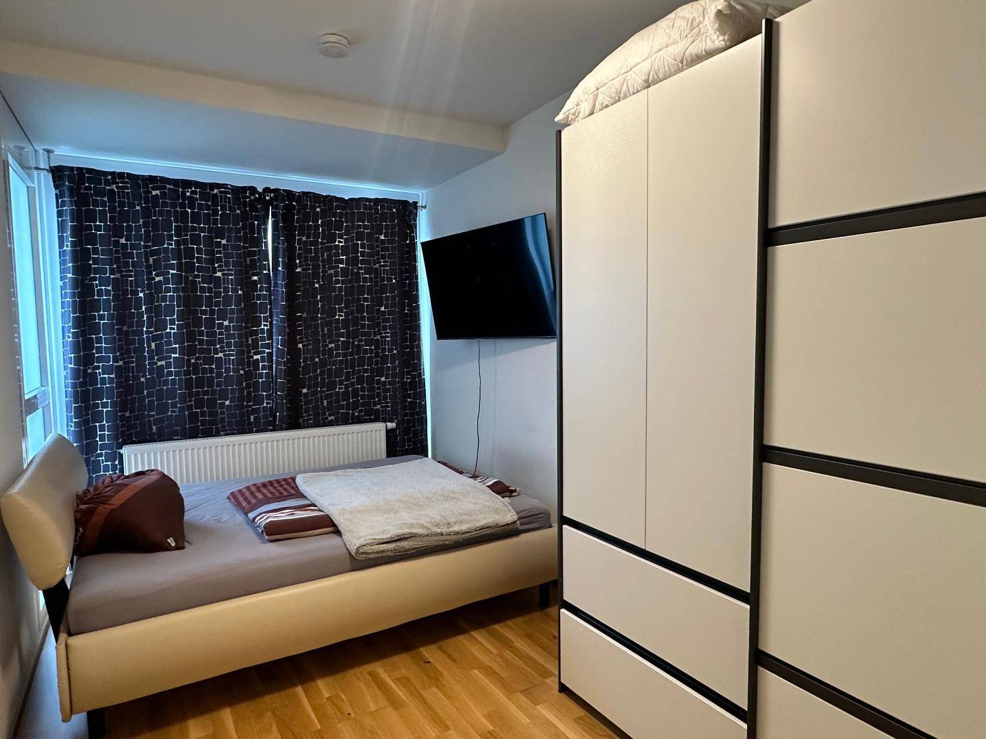 Schlafzimmer mit Einzelbett, Kleiderschrank und dunklen Vorhängen am Fenster.
