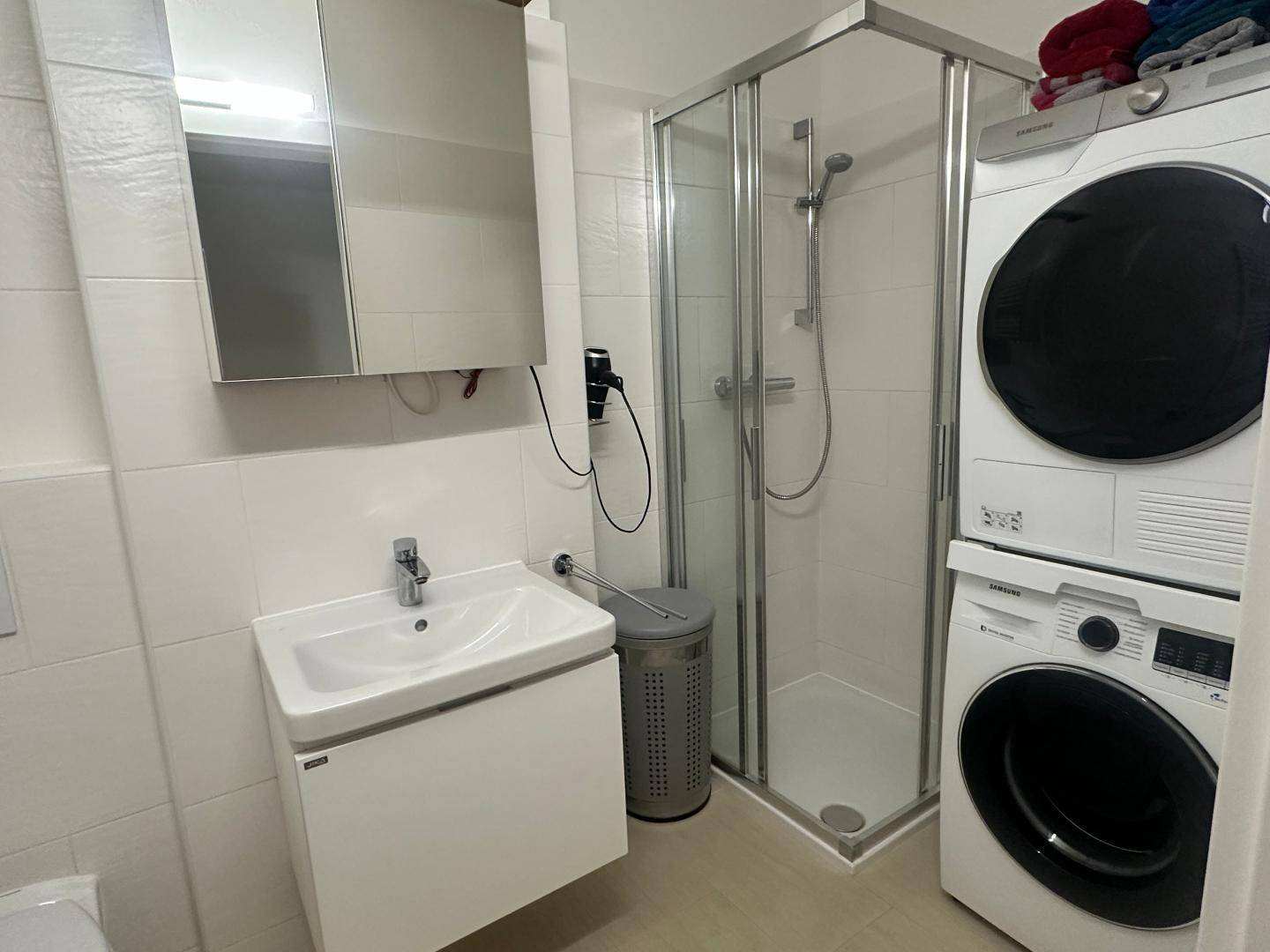 Modernes Badezimmer mit Dusche, Waschbecken und Waschmaschine sowie Trockner.