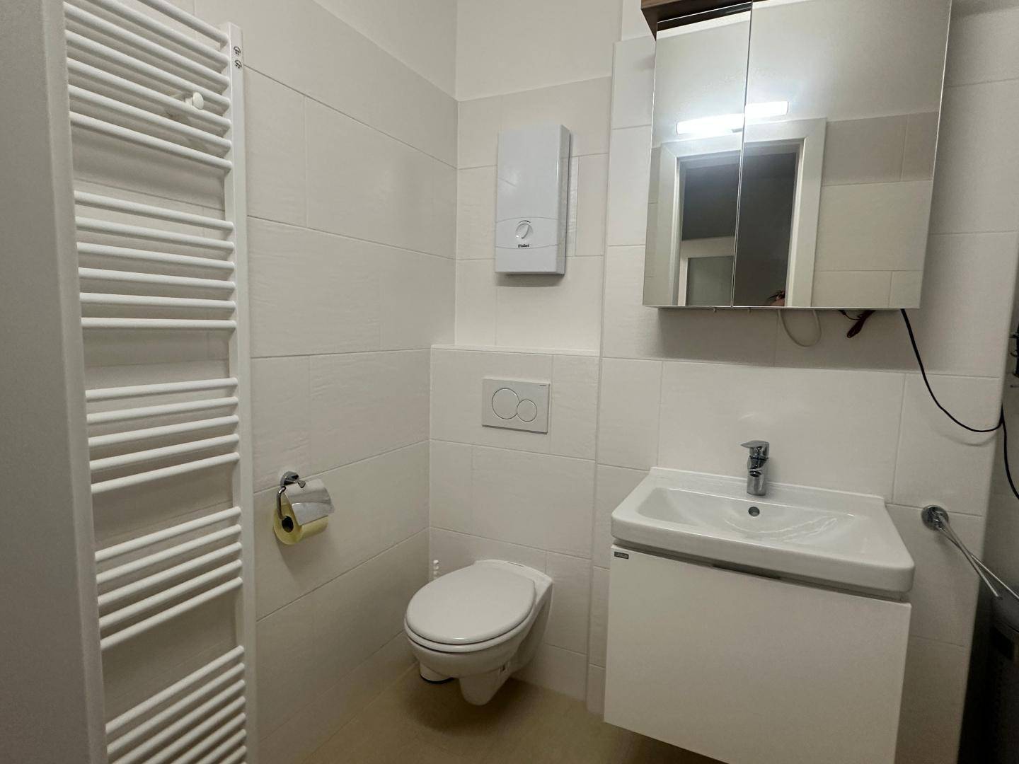 Separates WC mit wandhängender Toilette, Waschbecken und beheiztem Handtuchhalter.