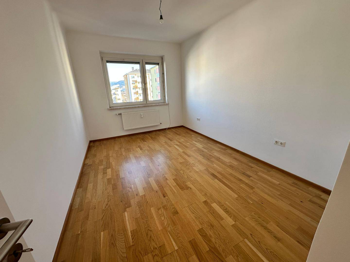 Helles Schlafzimmer mit Parkettboden und Fenster, das Tageslicht hereinlässt und eine Aussicht bietet.
