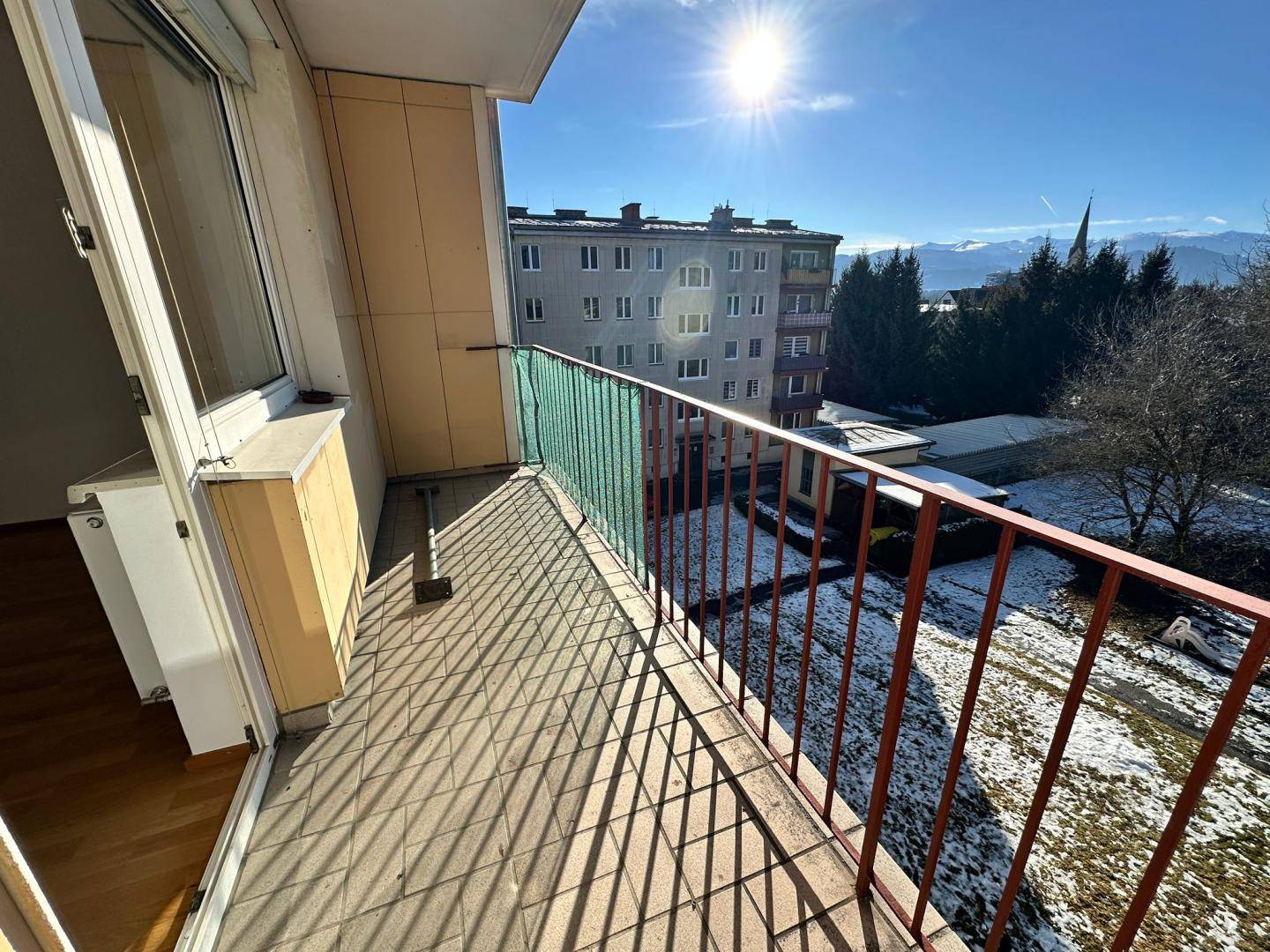 Balkon mit Metallgeländer und Blick auf die verschneite Umgebung und die Berge in der Ferne.