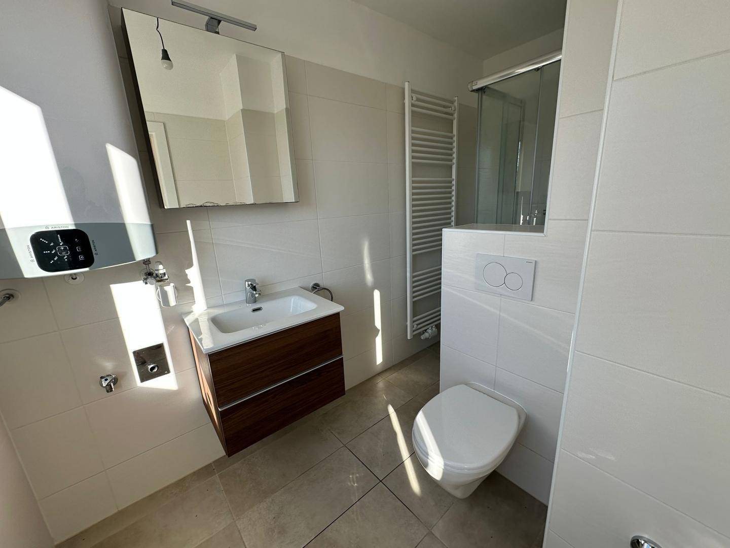Modern gefliestes Badezimmer mit Duschkabine, Waschbecken und Wand-WC, sehr gepflegt und hell.