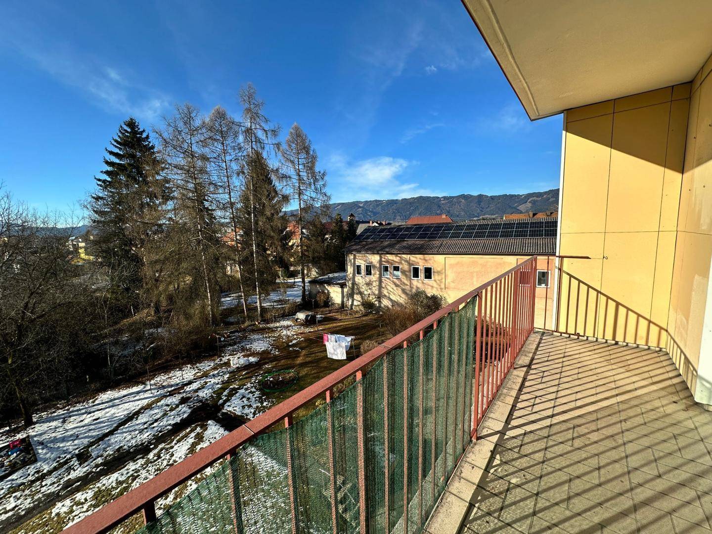 Balkon mit Blick auf die verschneite Umgebung und Bäume unter einem strahlend blauen Himmel.