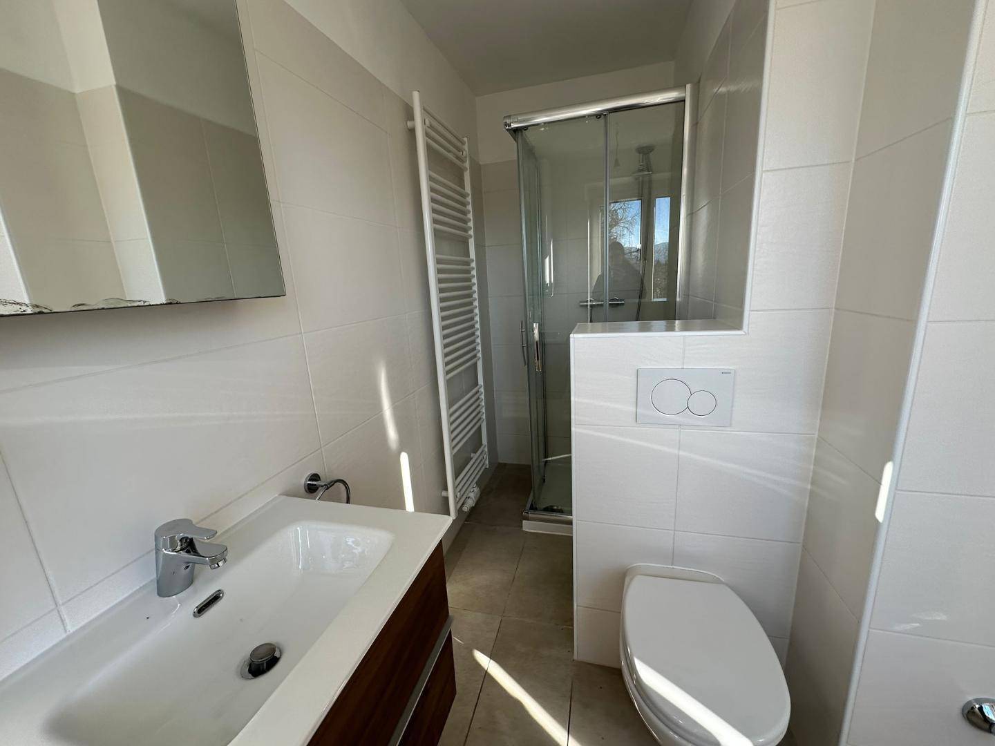 Modernes Badezimmer mit Dusche, WC, Einzelwaschbecken und beheiztem Handtuchhalter in Weiß.