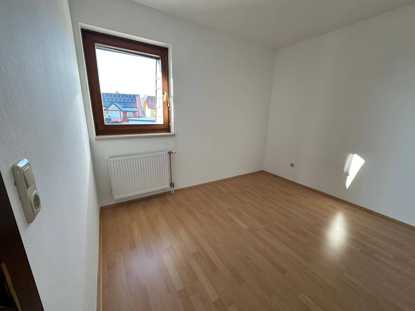 Helles, leeres Zimmer mit Laminatboden und einem Fenster, bereit zur individuellen Gestaltung.