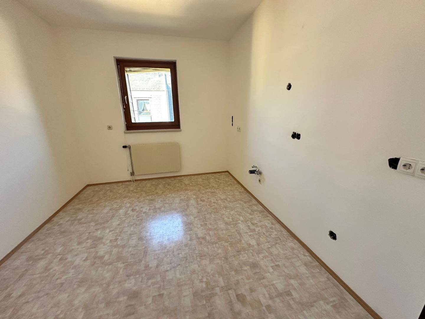 Leerer Raum mit Linoleumboden und Fenster, vorbereitet für eine Kücheninstallation.