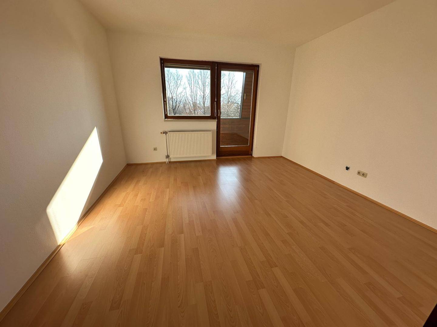 Geräumiges, helles Zimmer mit Laminatboden und Zugang zu einem Balkon.