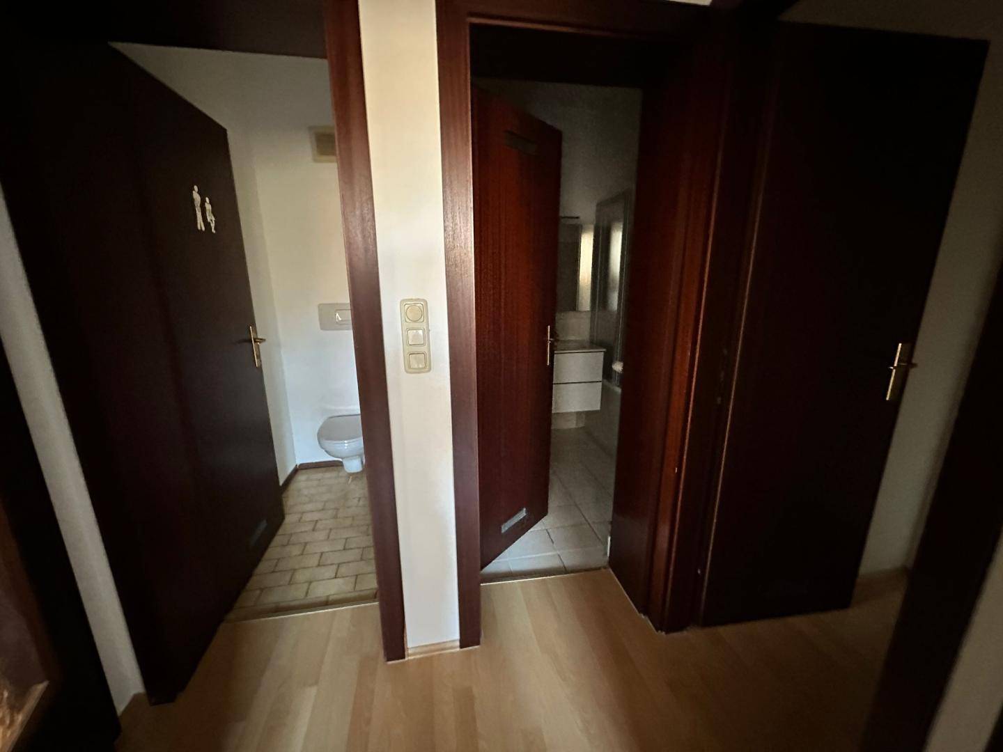 Flur mit dunklen Holztüren, der Zugang zu einem separaten WC und dem Badezimmer bietet.
