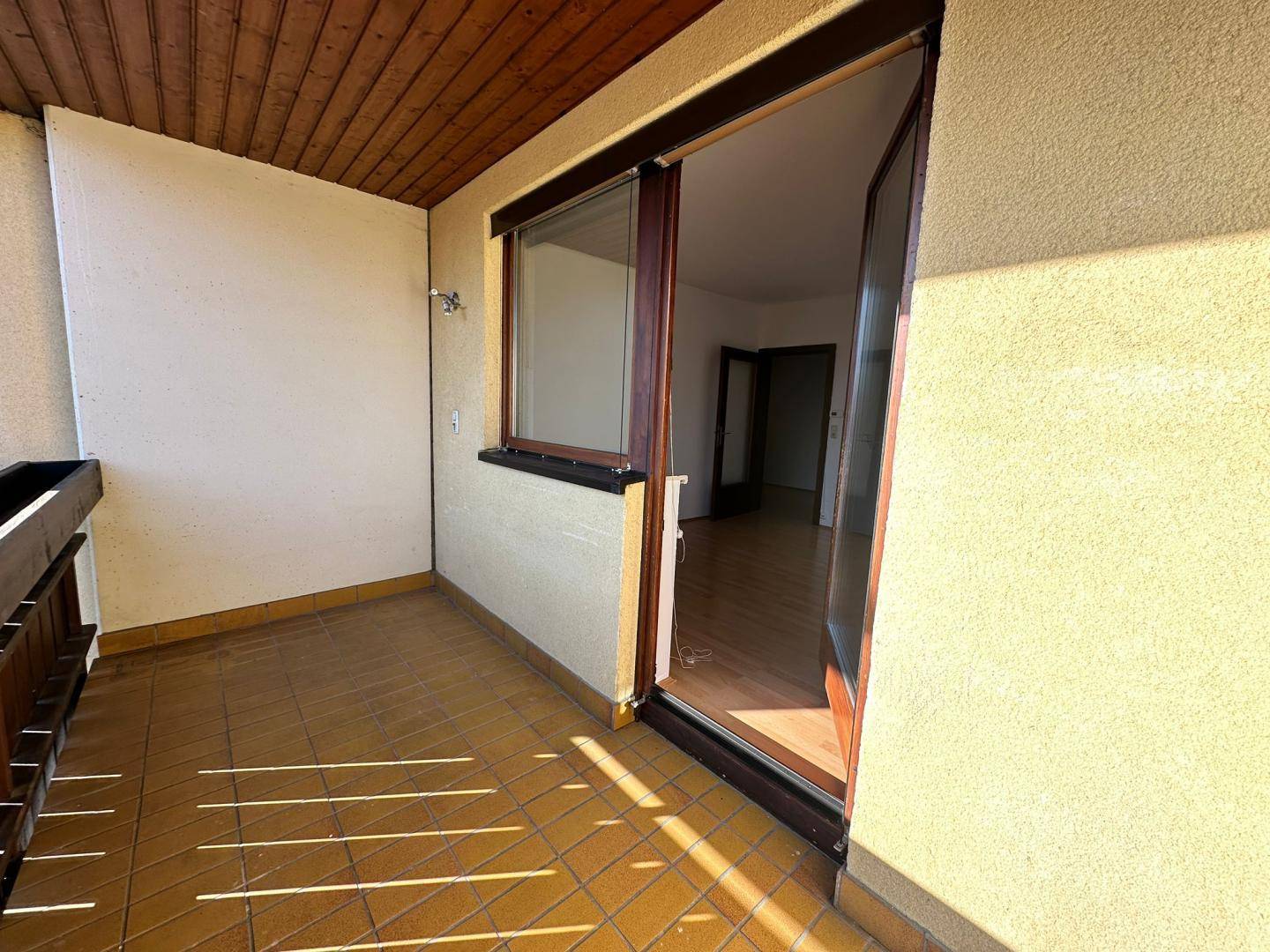 Geräumiger Balkon mit Fliesenboden und Holzelementen, direkter Zugang zum Innenbereich der Wohnung.