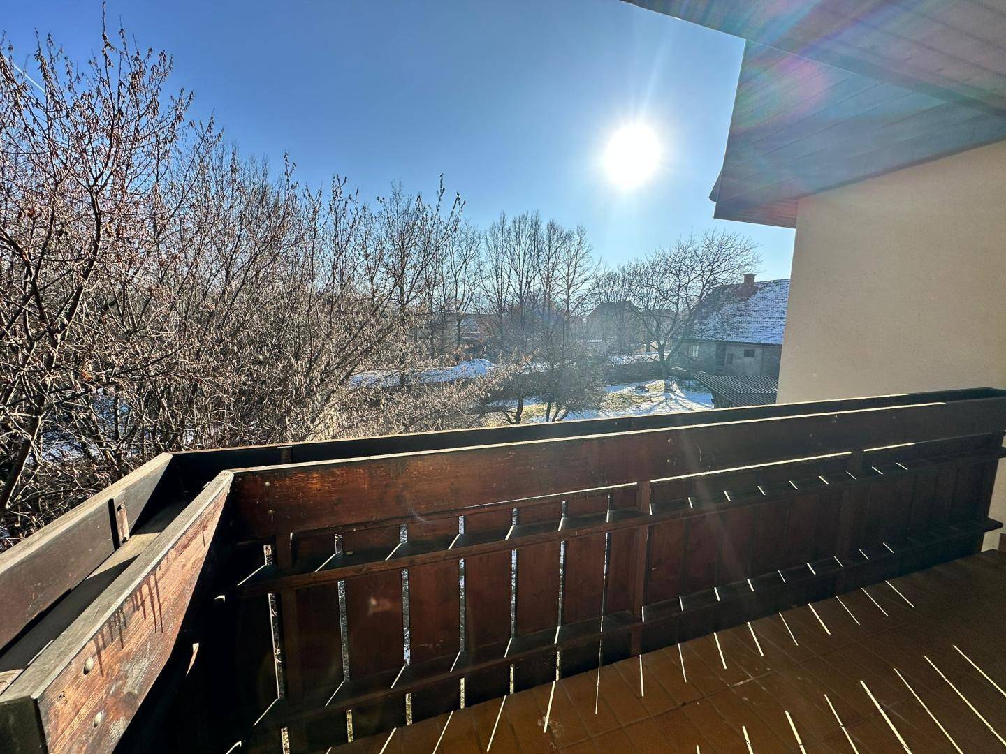 Sonniger Balkon mit Holzgeländer und weitem Blick über die verschneite Landschaft und Bäume.