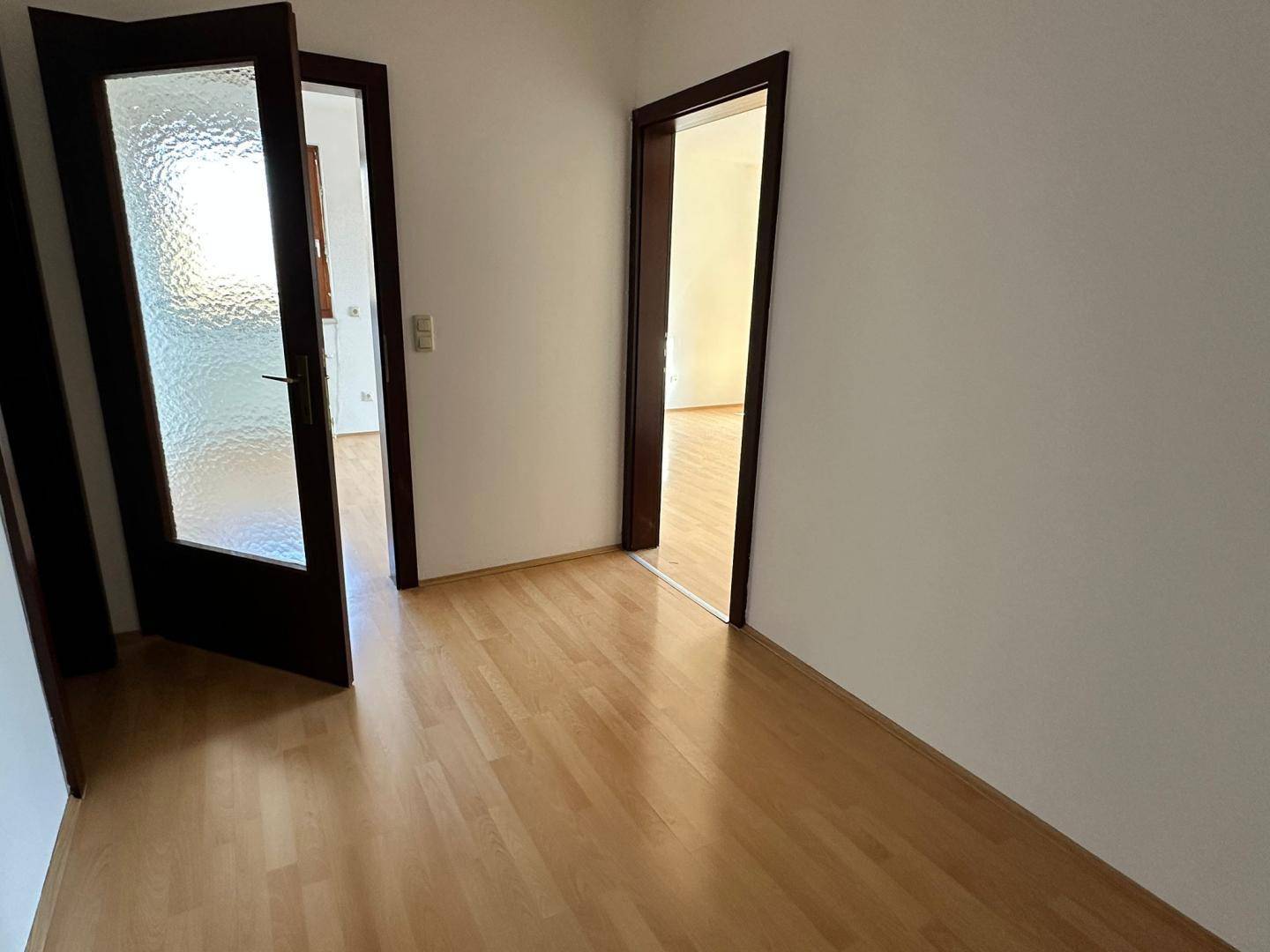 Heller Flur mit Holzboden und zwei offenen Türen, eine davon mit Milchglas, verbindet die Räume.