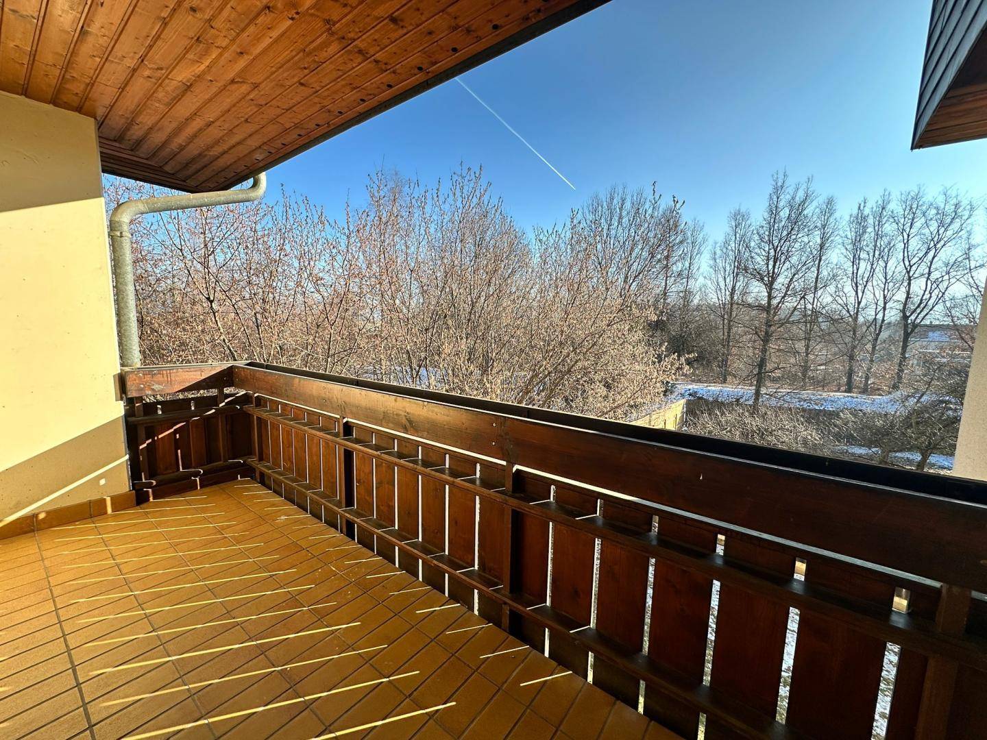 Sonniger Balkon mit Fliesenboden und Holzgeländer, bietet einen weiten Blick über die winterliche Landschaft.