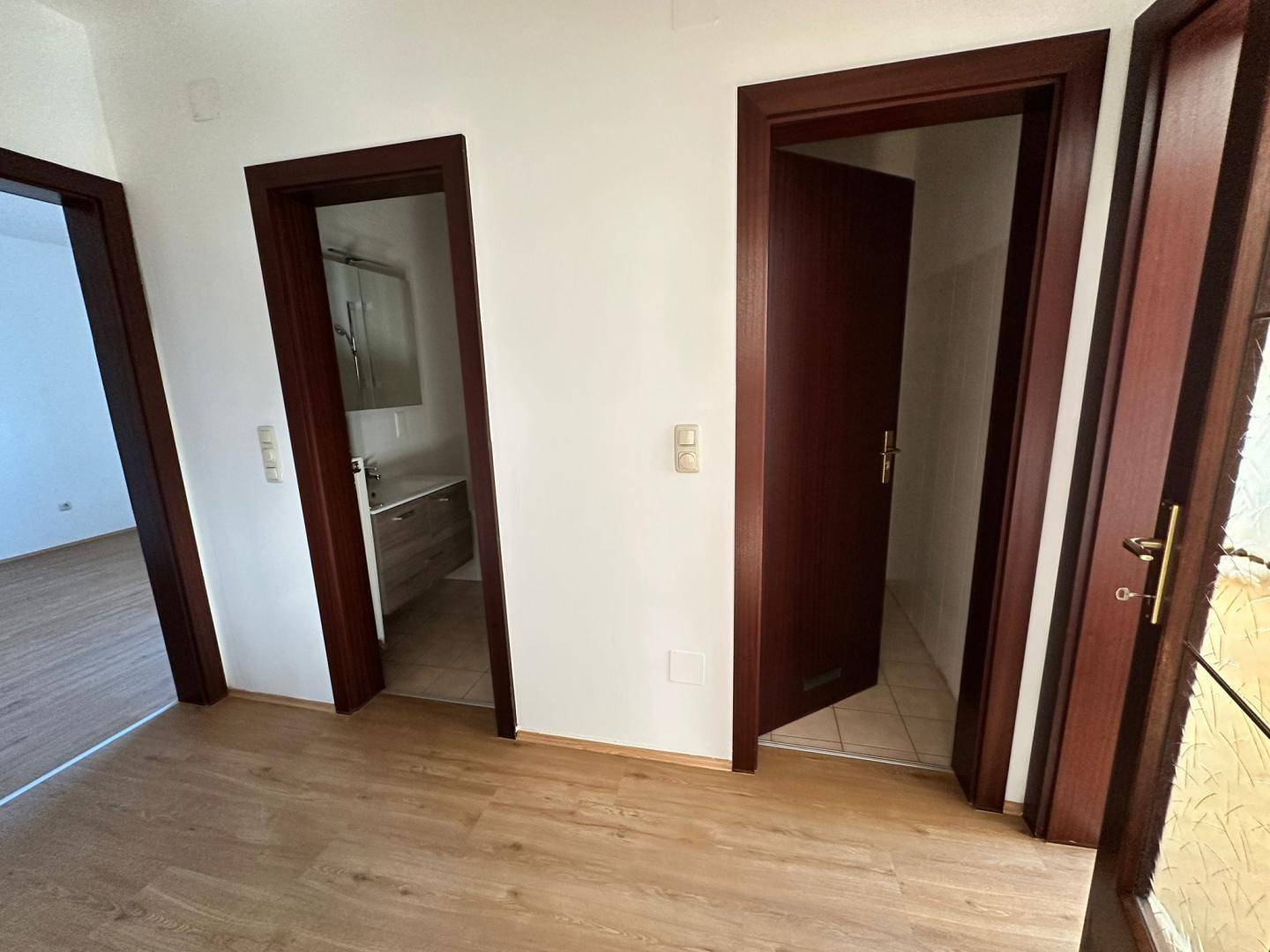 Heller Flur mit Laminatboden und mehreren dunklen Holztüren, die zu den Zimmern führen.
