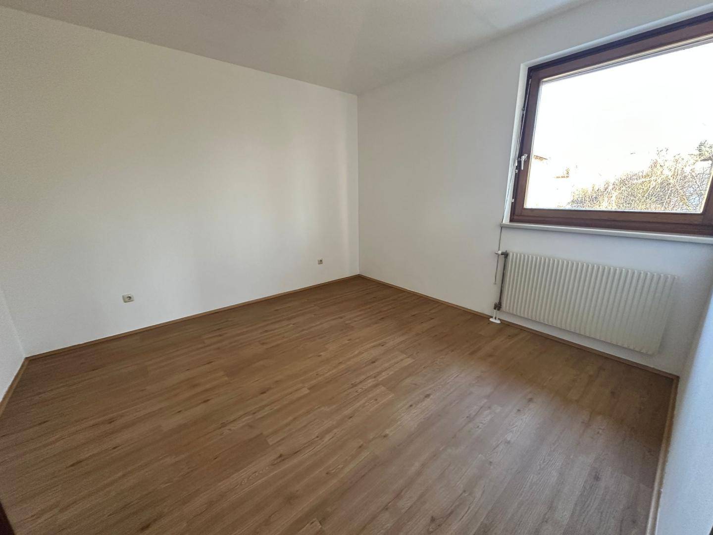 Freundliches Zimmer mit Laminatboden und einem Fenster, ideal als Schlaf- oder Arbeitszimmer.