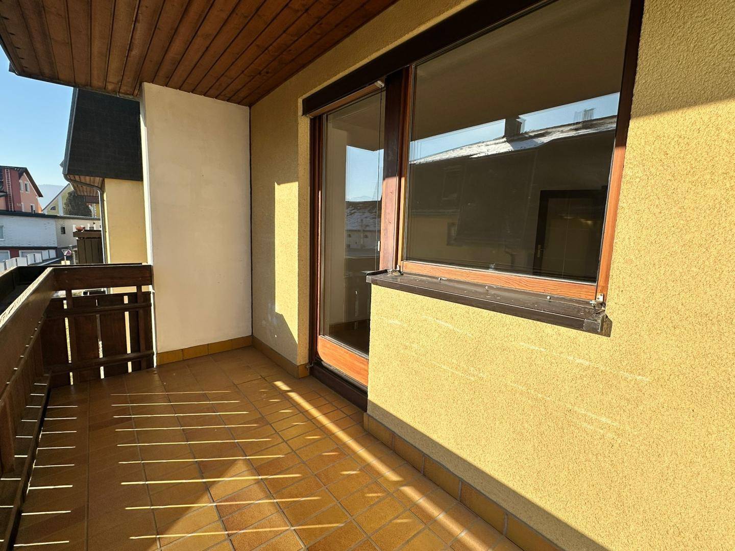 Sonniger Balkon mit Fliesenboden und Holzgeländer, bietet einen Blick auf die Umgebung.