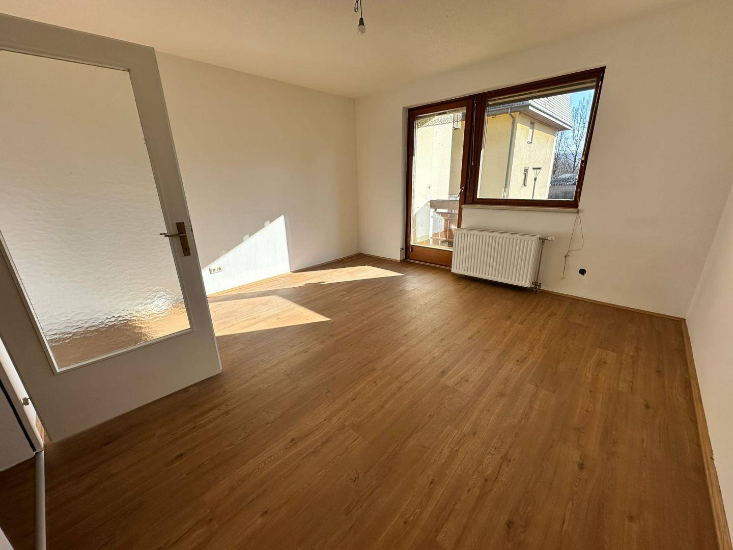 Helles Zimmer mit Laminatboden und Zugang zu einem kleinen Balkon, ideal als Wohn- oder Schlafzimmer.
