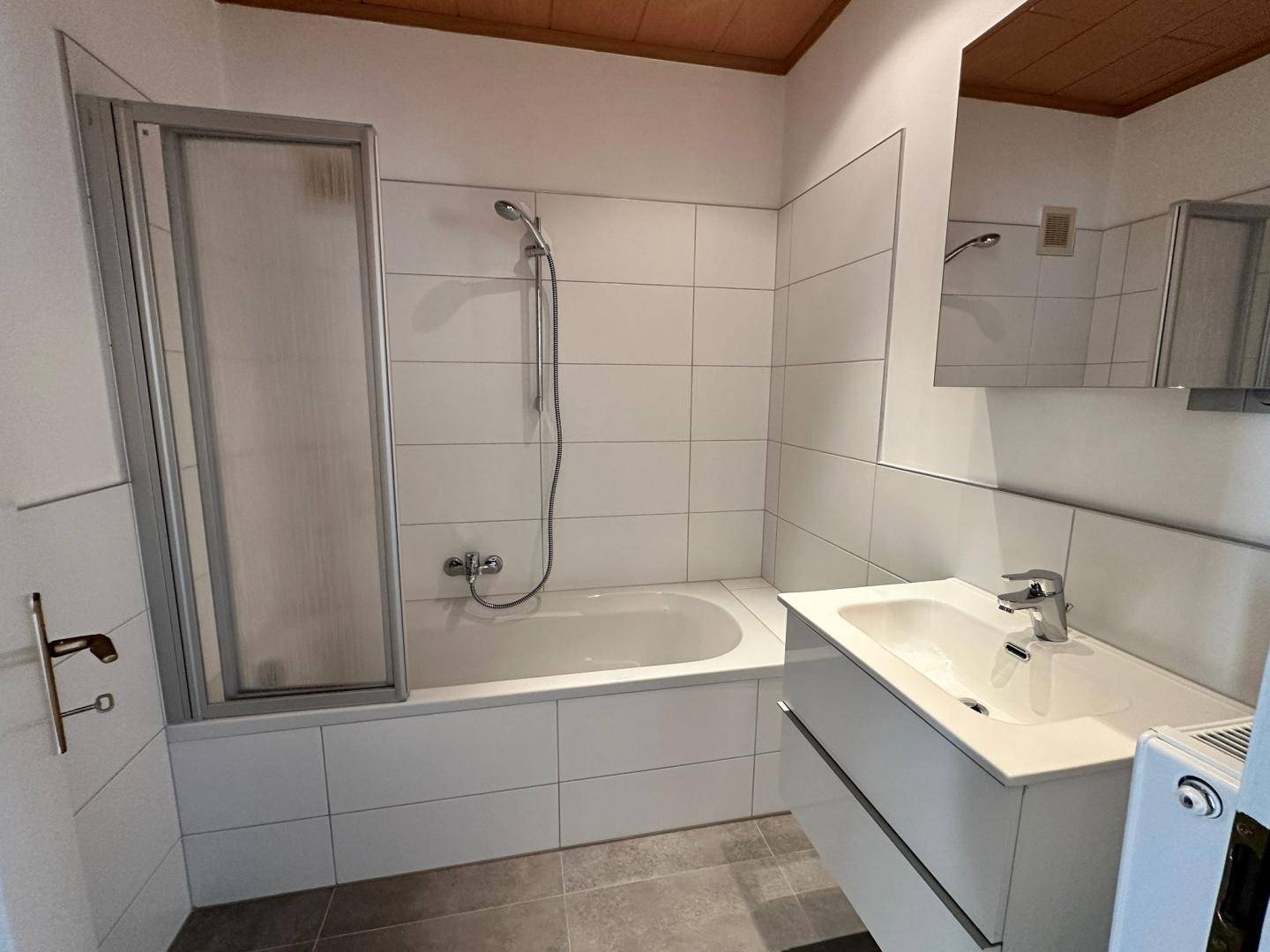 Modernes Badezimmer mit Badewanne, Duschabtrennung, Waschbecken und Spiegelschrank.