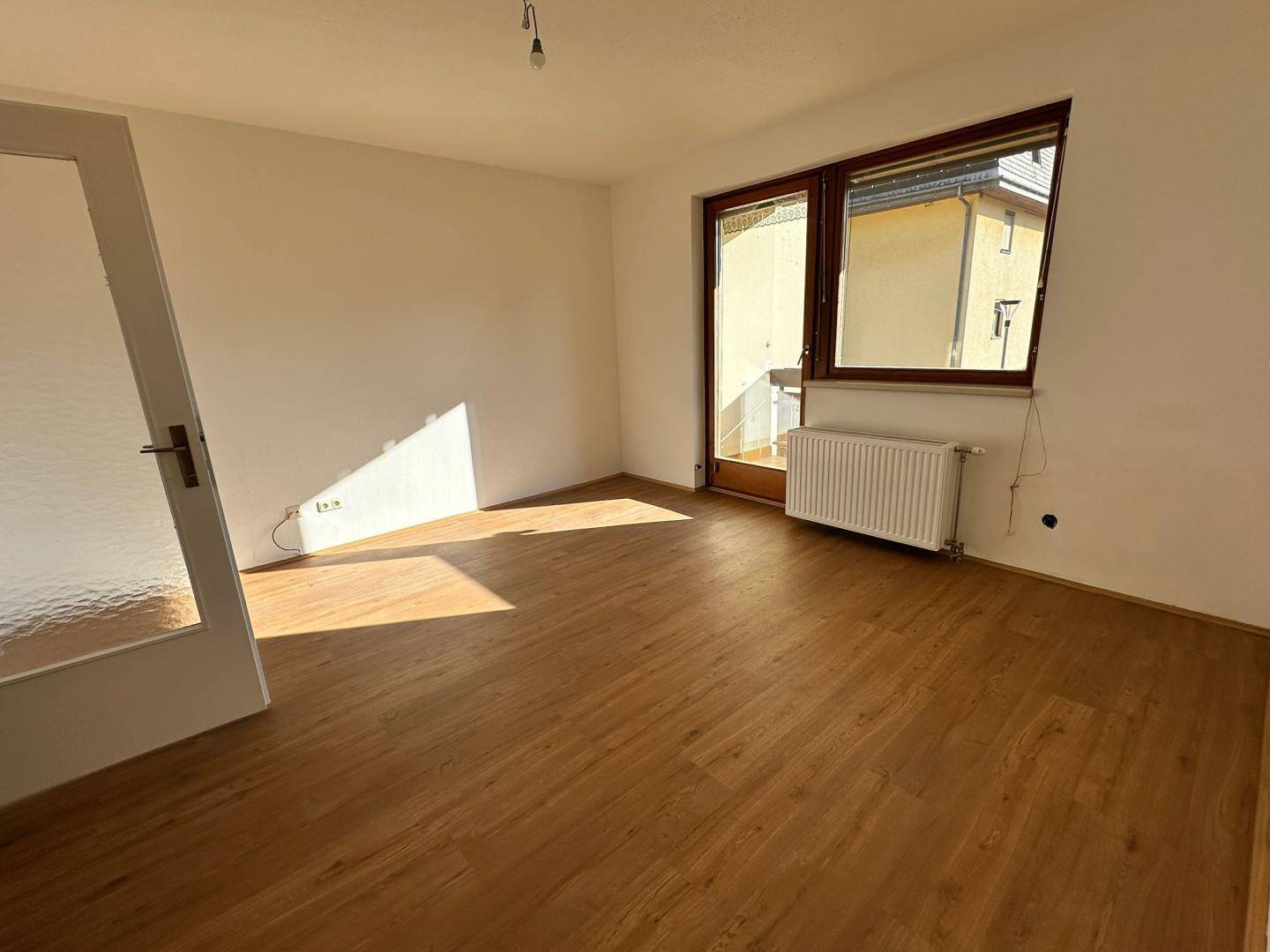 Lichtdurchflutetes Zimmer mit Laminatboden und Zugang zu einem Balkon, ideal als Wohnbereich.