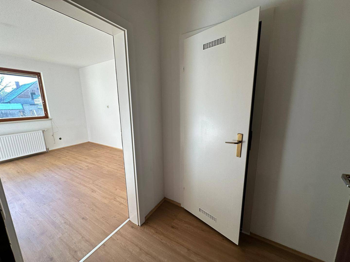 Heller Flur mit Laminatboden und weißer Tür, die in einen weiteren Raum führt.
