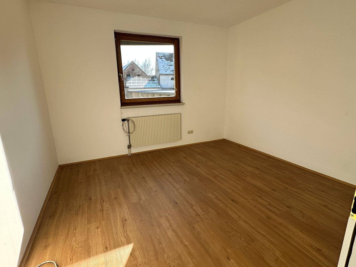 Ruhiges Zimmer mit Laminatboden und Fenster, das sich gut als Schlaf- oder Arbeitszimmer eignet.