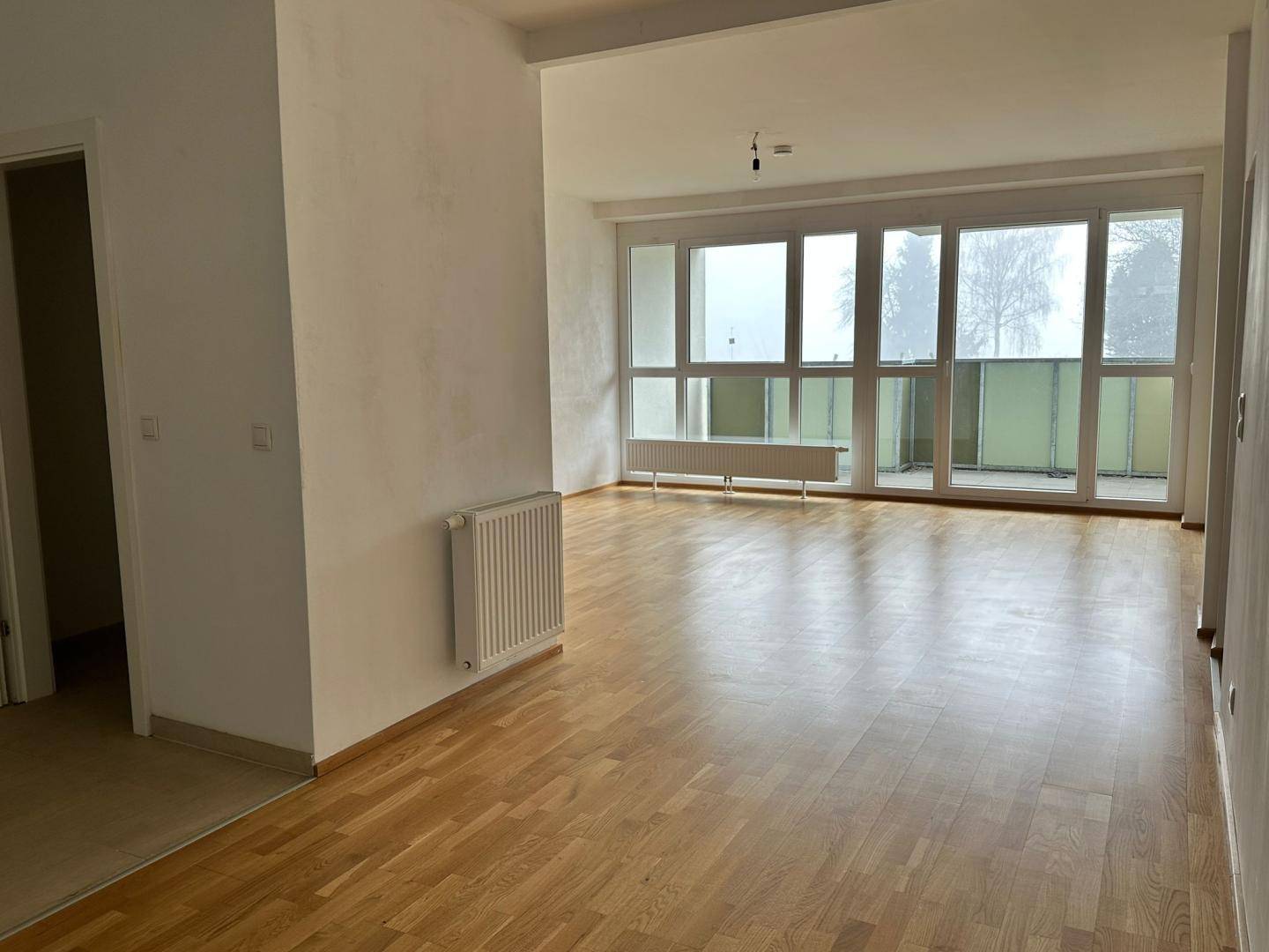 Geräumiger Wohnbereich mit hellem Parkettboden und großen Fenstern zum Balkon.
