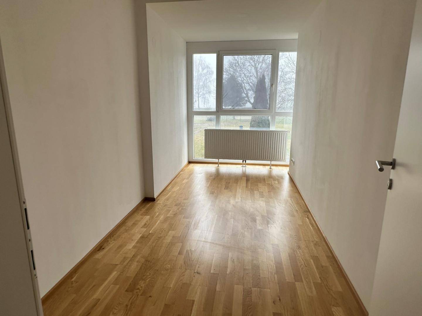 Geräumiges Zimmer mit Parkettboden und hoher Fensterfront für viel Tageslicht.
