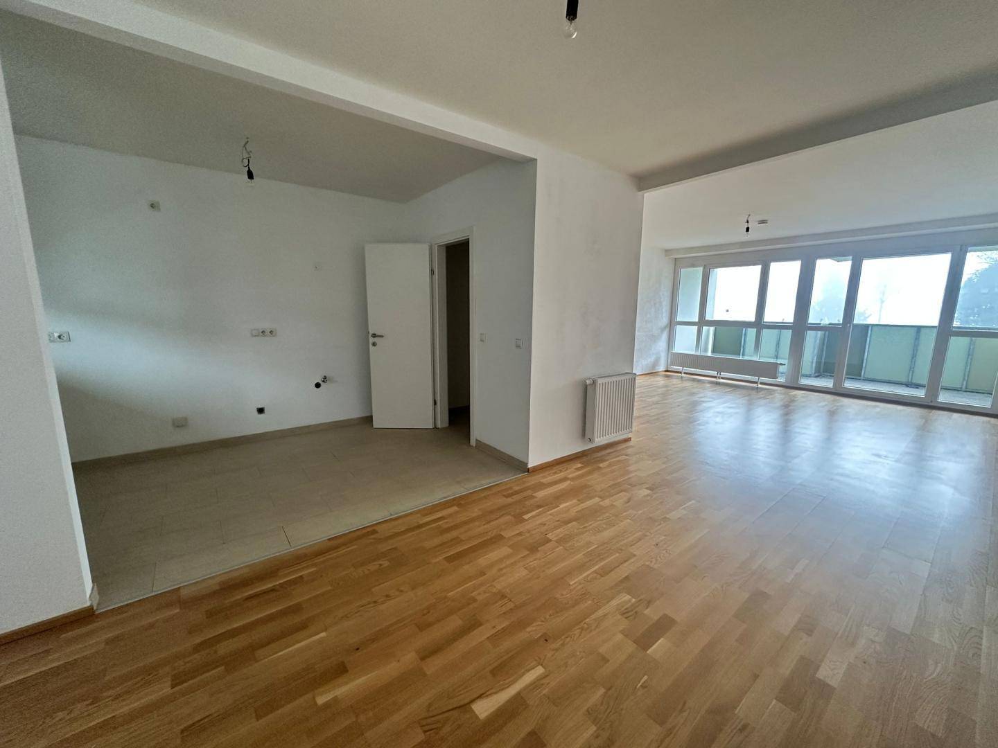 Heller Wohnbereich mit Parkettboden und Zugang zu einem Balkon, teilweise gefliest.