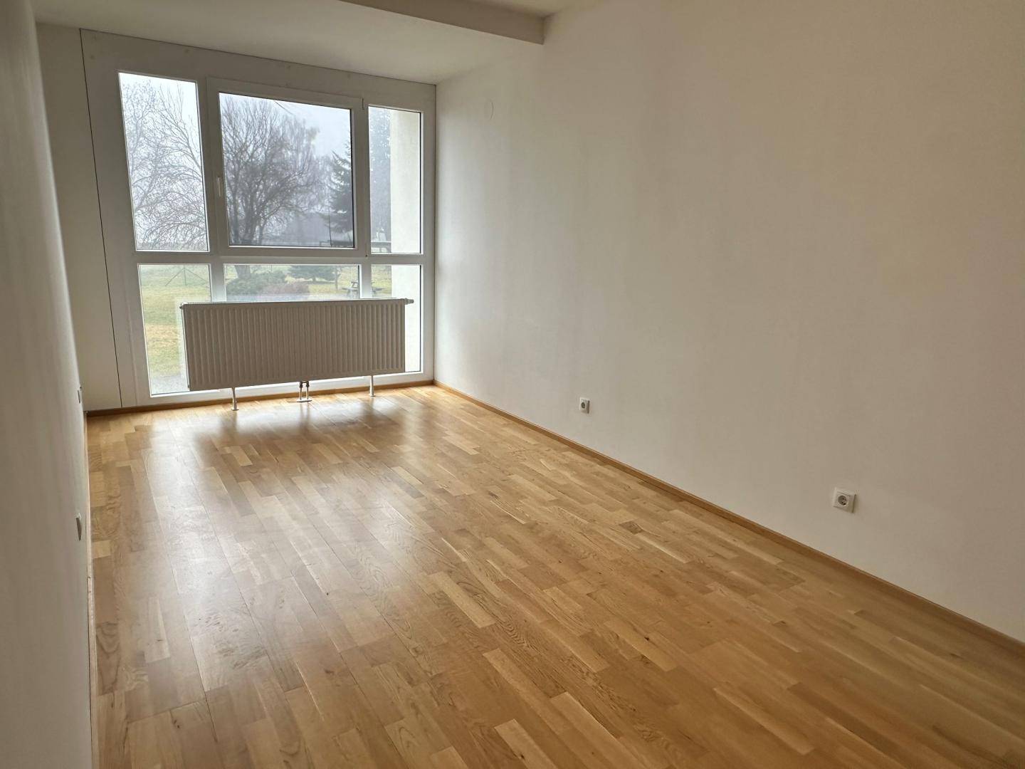 Helles Schlafzimmer mit Parkettboden und großem Fenster, das eine weite Aussicht bietet.